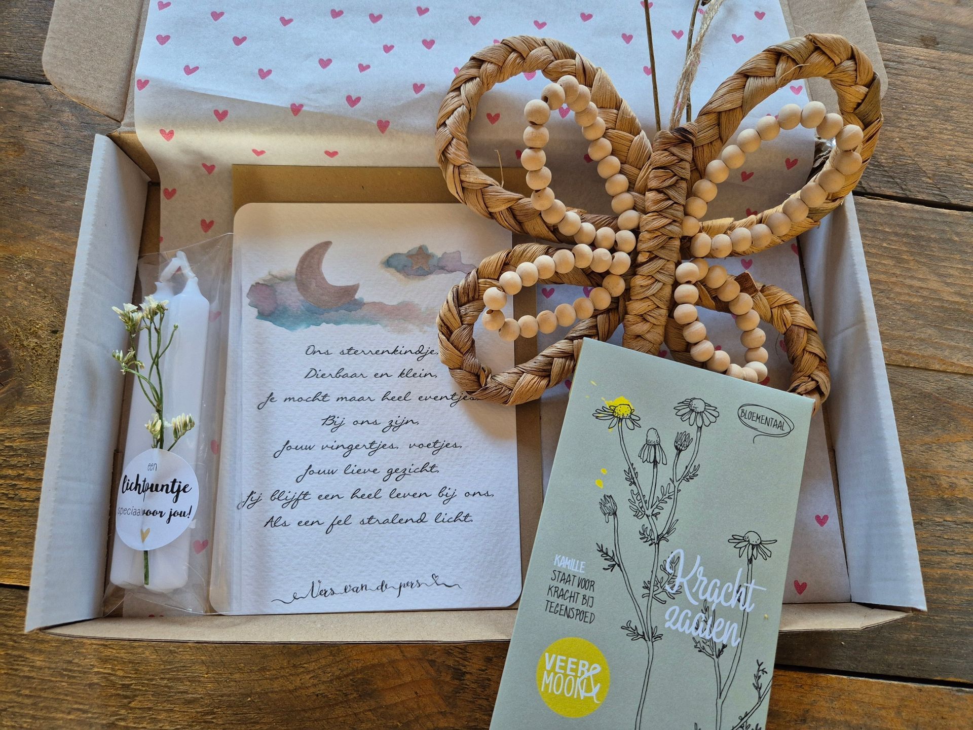 Doos met een kaartje, vlinderdecoratie, een zakje zaadjes en een kaars. De binnenkant van de doos is versierd met roze hartjes.