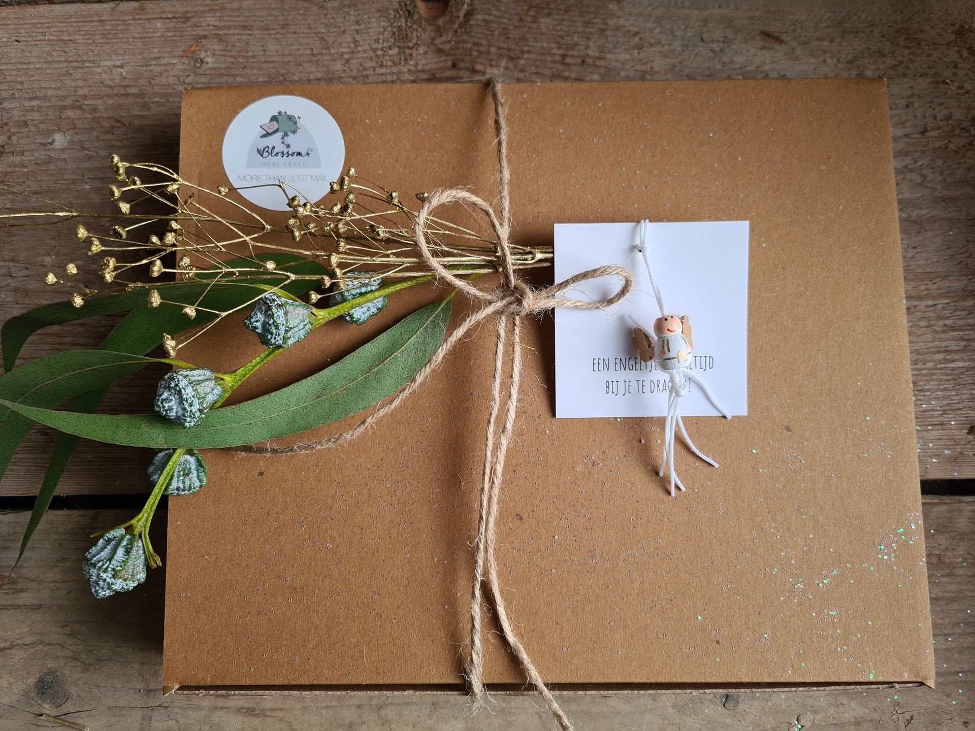 Een ingepakt bruin pakketje, vastgebonden met touw, versierd met bloemen en een klein labeltje op een houten ondergrond.