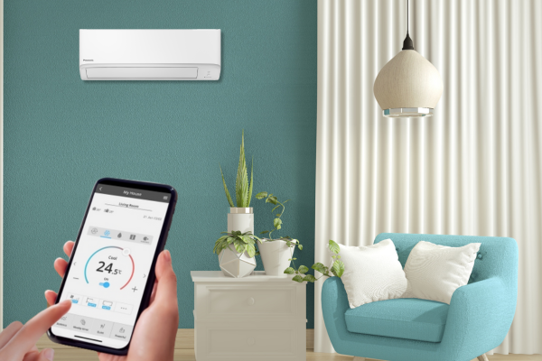 Hand holding phone controlling wall-mounted air conditioner in a teal room.