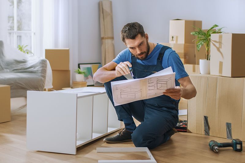 A man is kneeling down in a living room while looking at a blueprint.