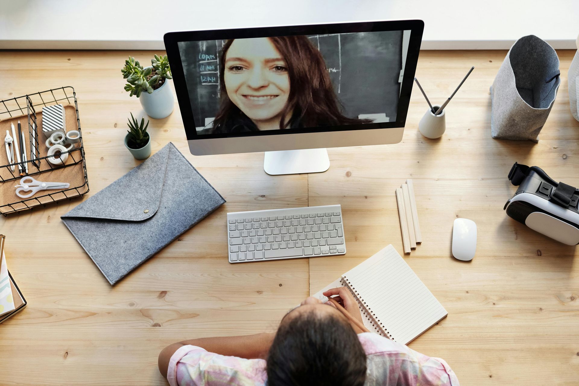 Person at desk on a video call, looking at the screen. Desktop computer, notepad, and desk accessories.