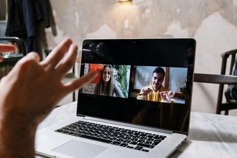 Person using laptop, video call with two people smiling, hand gesture of peace.