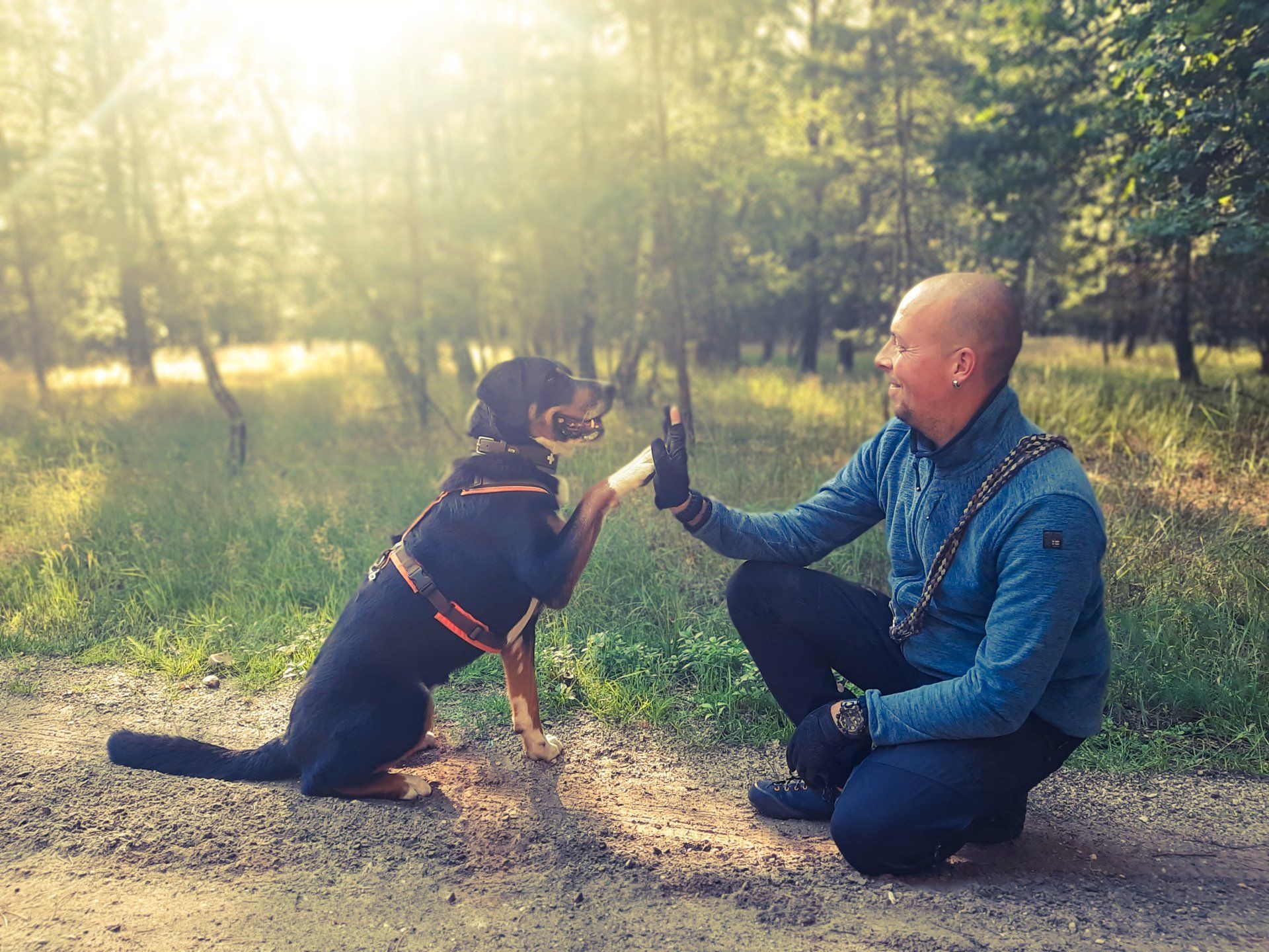 Oliver Kluge kniet neben seinem Hund Elli und gibt ihr ein High Five.