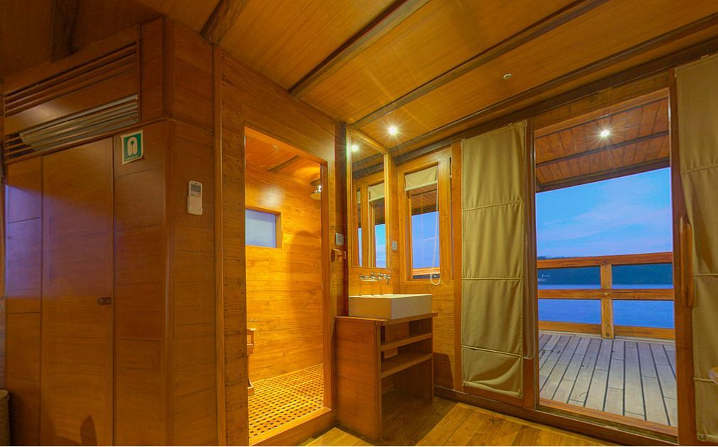 Wooden bathroom with a shower, vanity, and large sliding doors leading to a deck overlooking water.