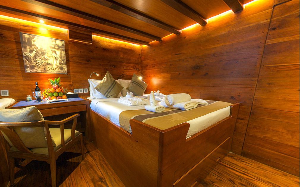 Wooden cabin interior with bed, desk, artwork, and fruit.