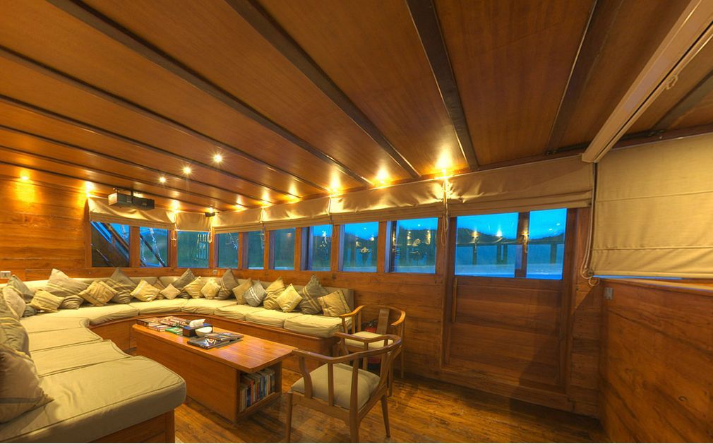 Interior of a wooden boat with a curved sofa, windows, and warm lighting.