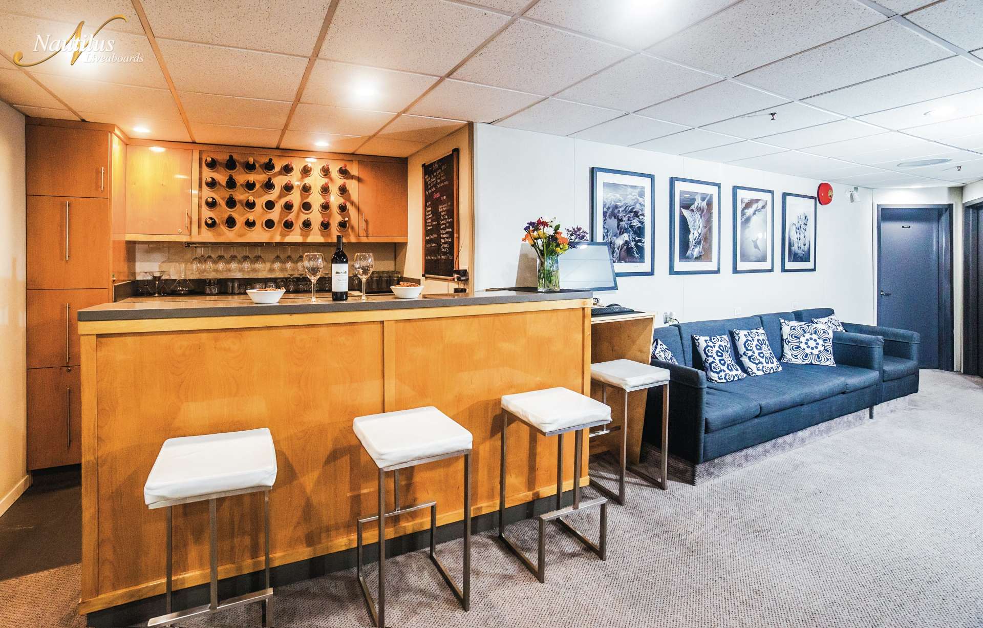 Basement bar with wooden counter and stools, wine rack, and seating area with sofa and framed photos.