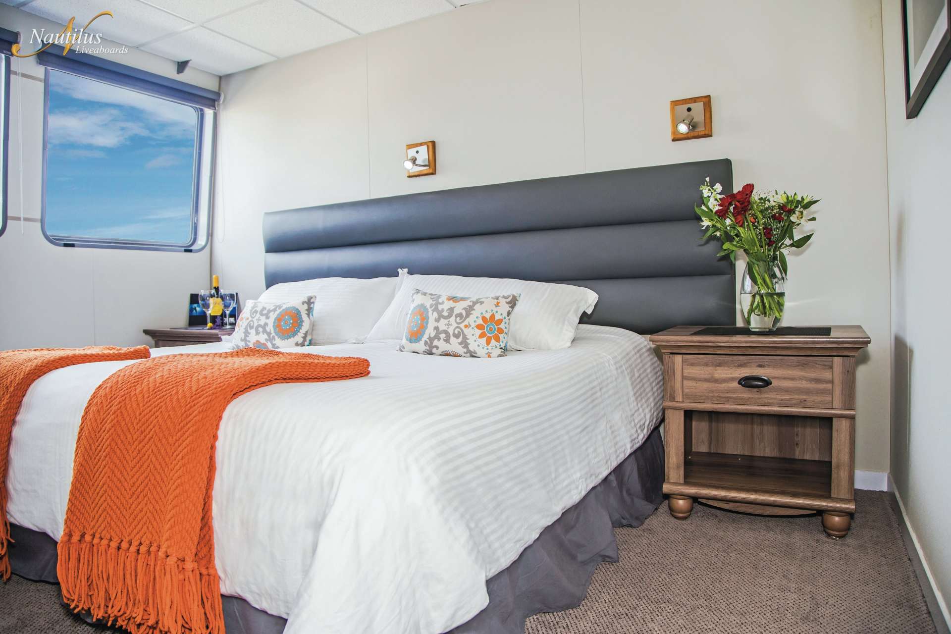 Bedroom with a white bed, orange throw, and a blue-sky window view.