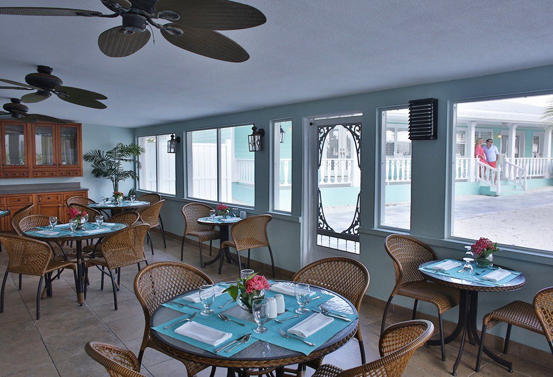 Restaurant dining room with round wicker tables, blue place settings, and large windows.