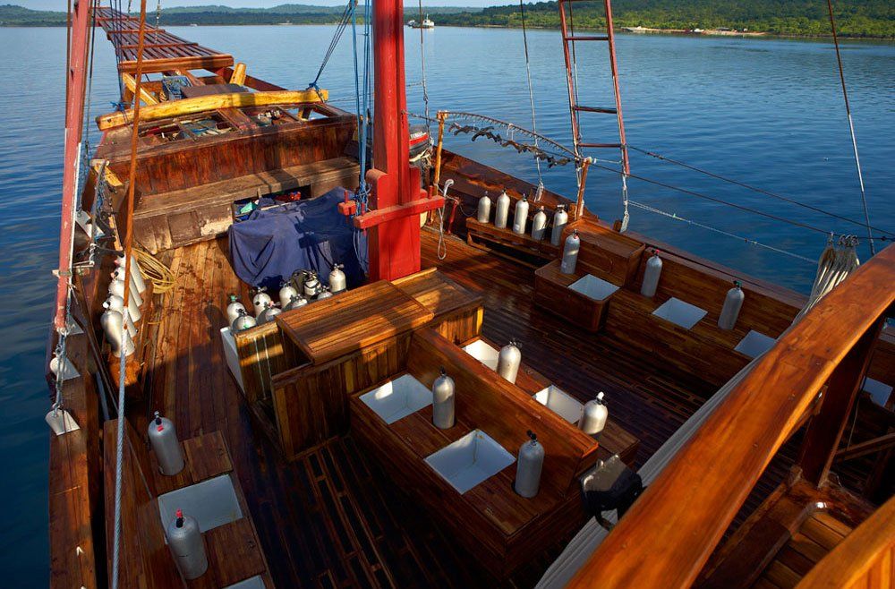 Wooden dive boat with scuba tanks, blue water and a forested shoreline in the background.
