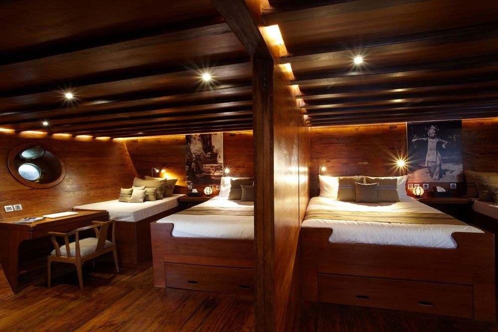 Wooden ship cabin interior with beds, desk, porthole, and warm lighting.