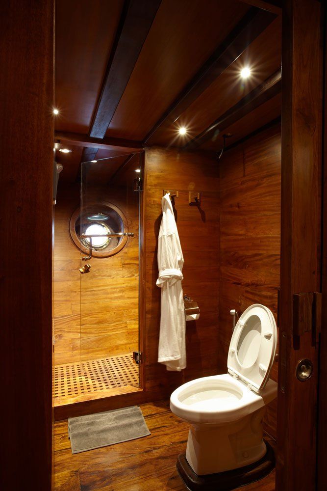 Wooden bathroom on a boat with a toilet, shower, and robe hanging on the wall.