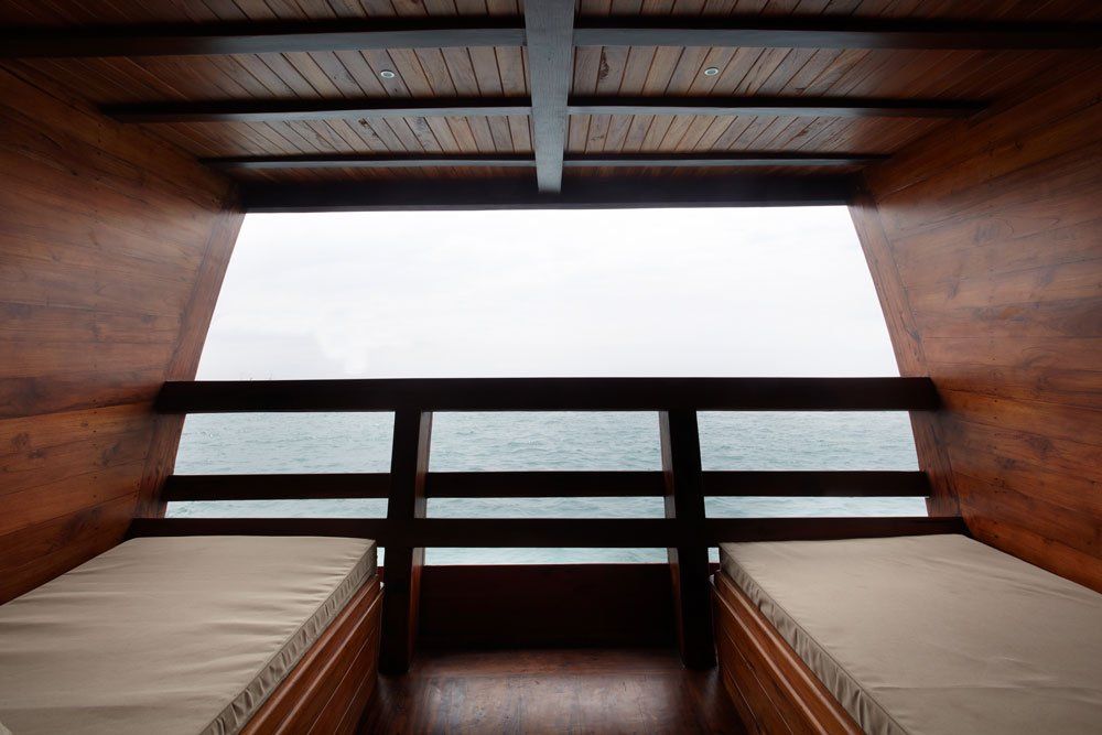 Interior view of a wooden boat cabin with two beds facing an ocean view.