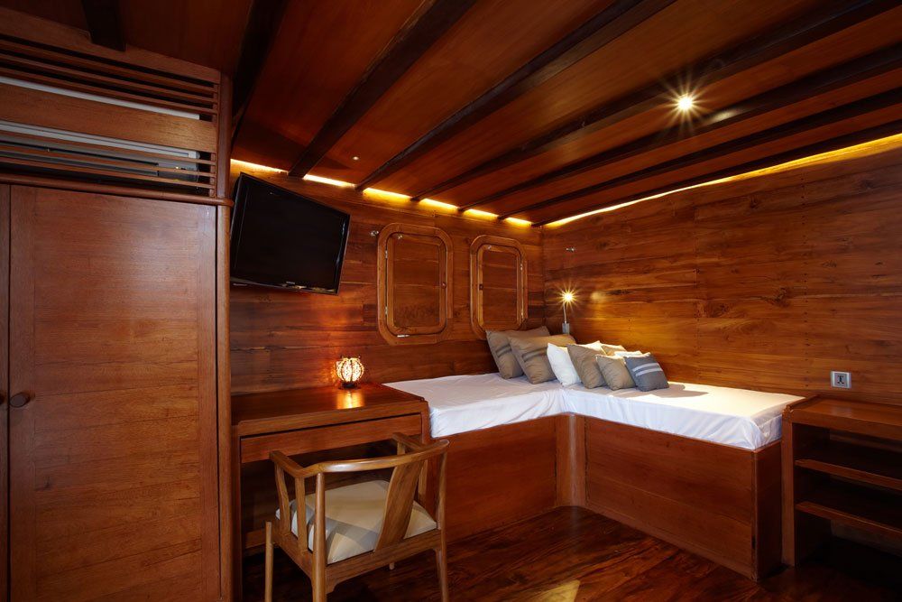 Wooden ship cabin with a bed, desk, and TV.
