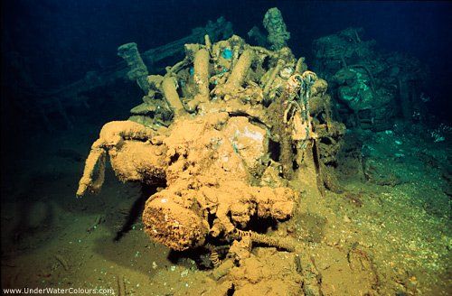 Underwater view of a corroded aircraft engine covered in marine growth on the ocean floor.