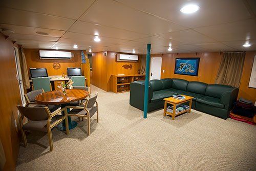 A cozy interior with a round table, a green sectional sofa, and computer desks.