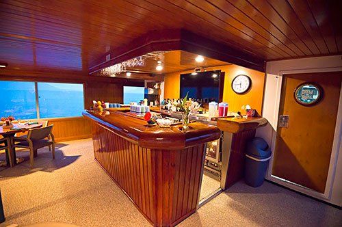 Wooden bar with stools and drinks, on a boat with water view.
