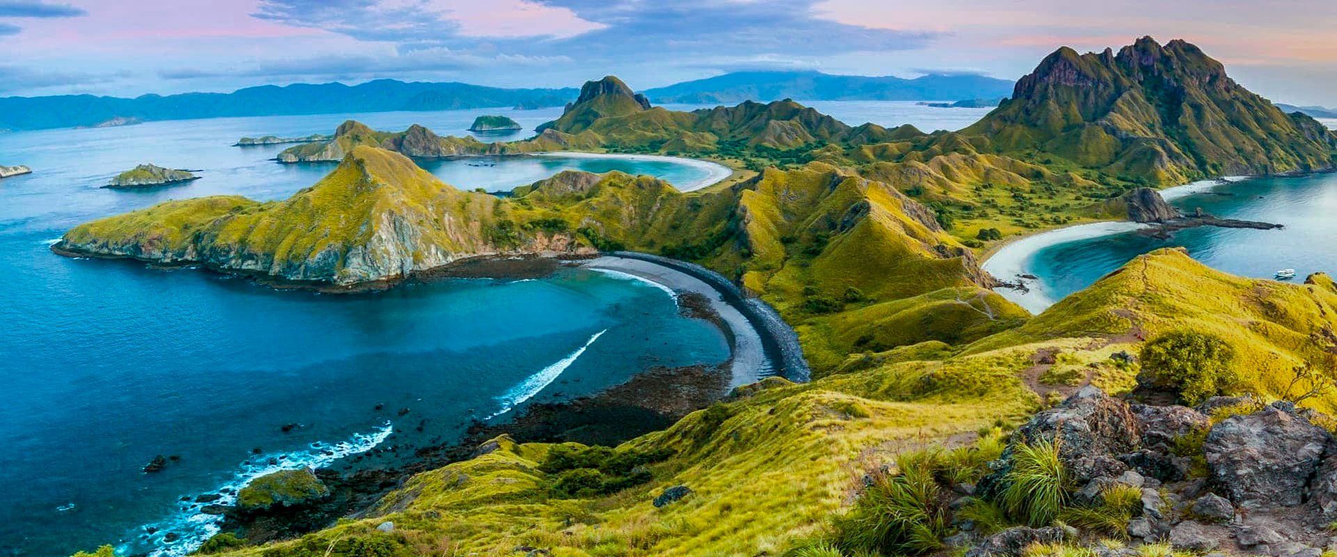 Panoramic view of a tropical island with lush green hills, turquoise waters, and a dark sandy beach.