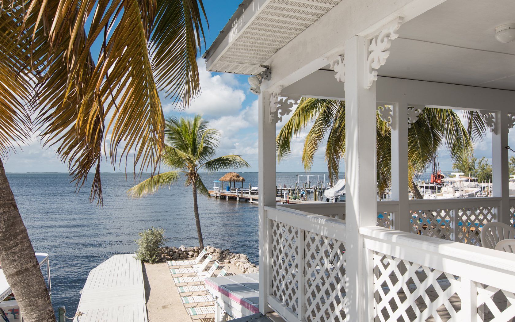 White cottage overlooking water and dock; palm trees frame the view.