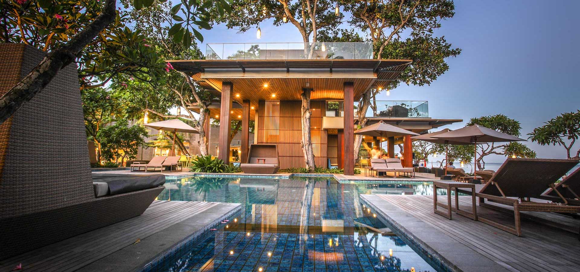 Swimming pool with lounge chairs, umbrellas, and a wooden structure with lights.