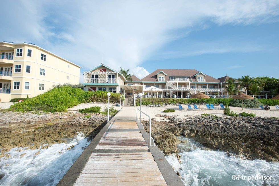 Wooden pier leading to beach with buildings under a blue sky. Waves crash on rocks.