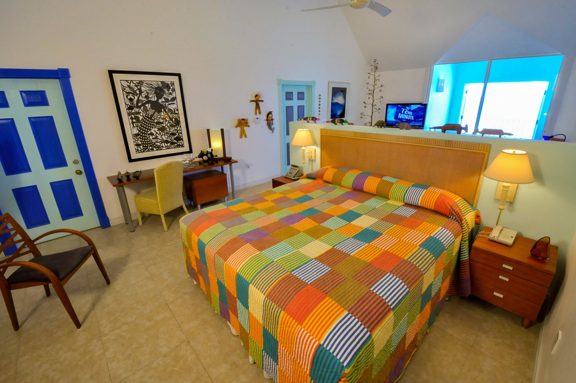 Bedroom with a colorful patchwork quilt on the bed, blue door, and art on the wall.