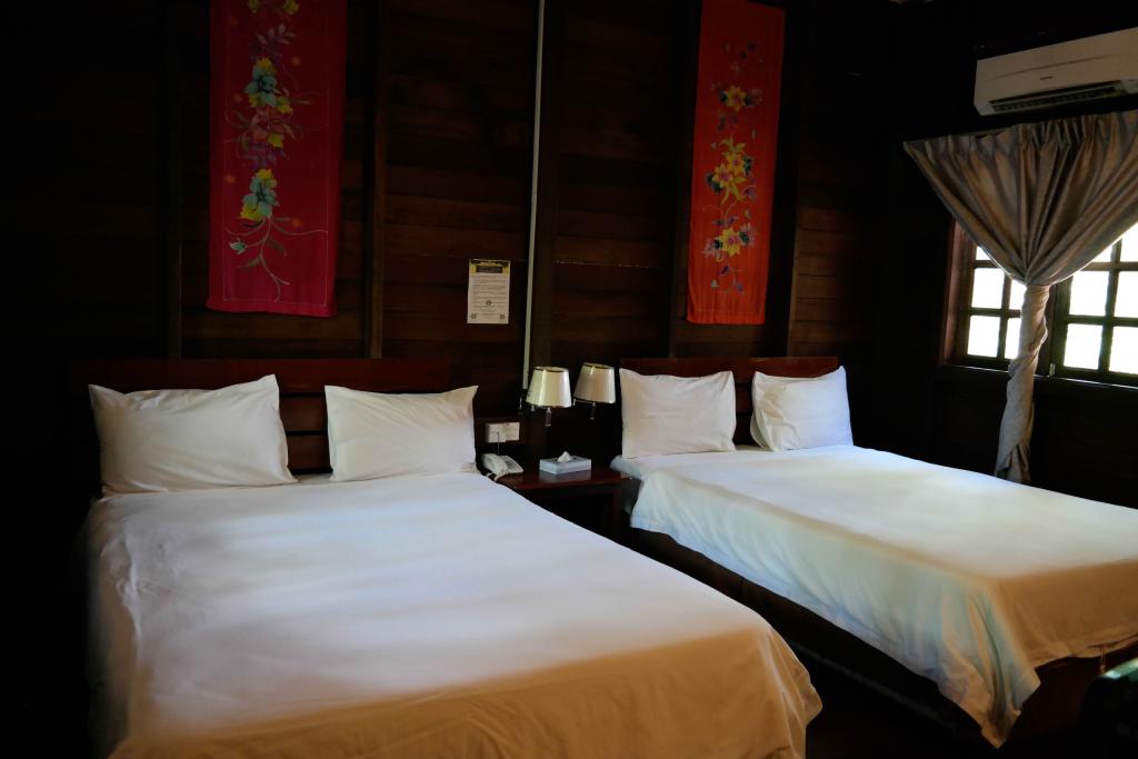 Two beds in a dark-paneled room, with white linens. Decorative wall hangings and a window with a curtain.