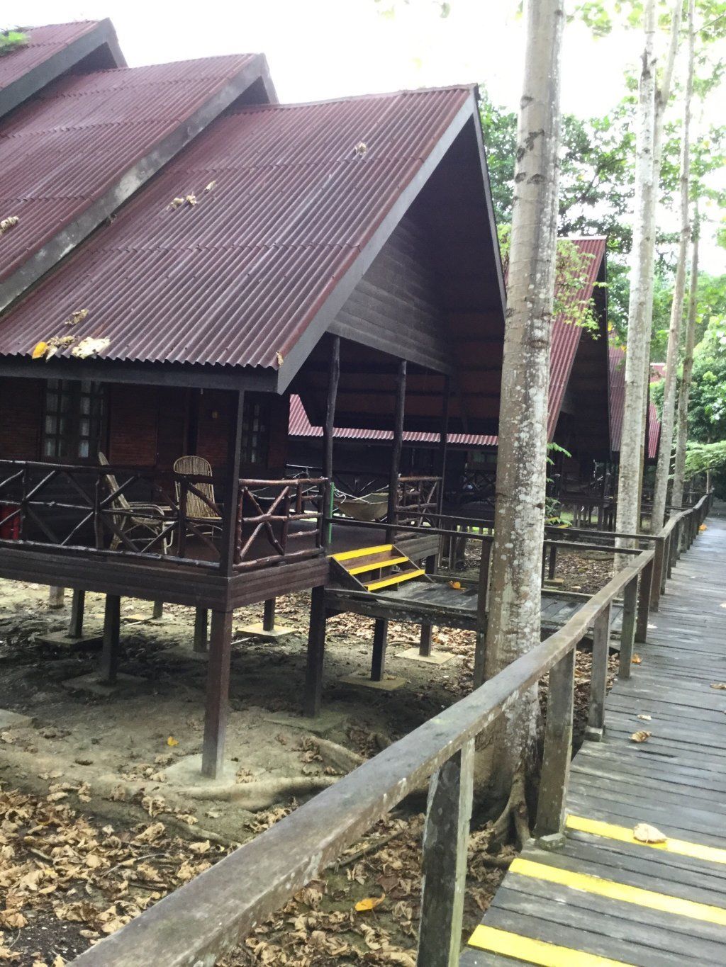 Wooden cabins on stilts with a covered walkway. Brown, red, and beige colors.