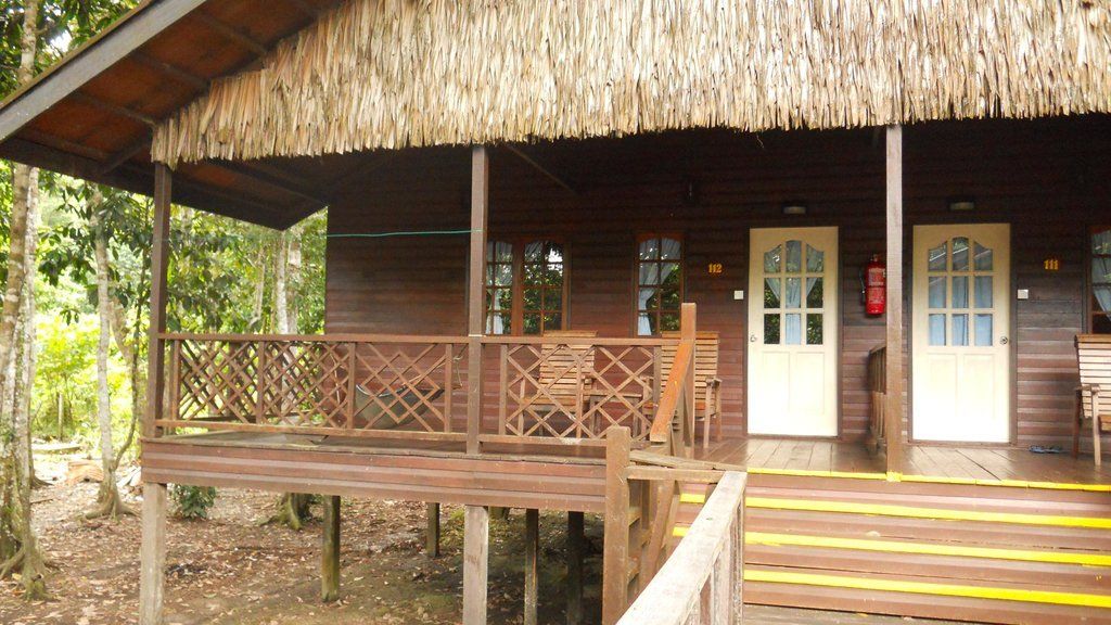 Wooden cabin with thatched roof, porch, and two doors. Located in a natural setting.