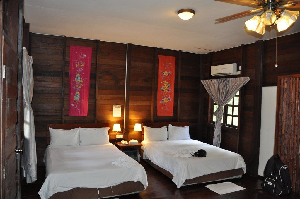 Two beds in a wood-paneled room, with colorful wall hangings and a ceiling fan.