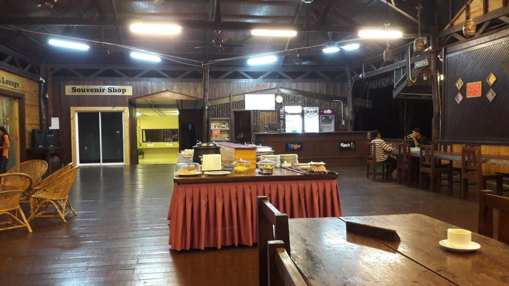 Interior of a restaurant with buffet table, wooden tables/chairs, and a bar.