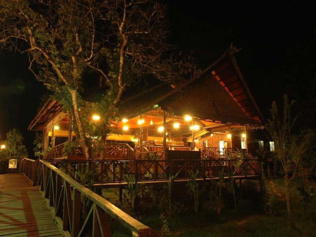 Wooden restaurant at night with warm lights, a bridge, and trees.