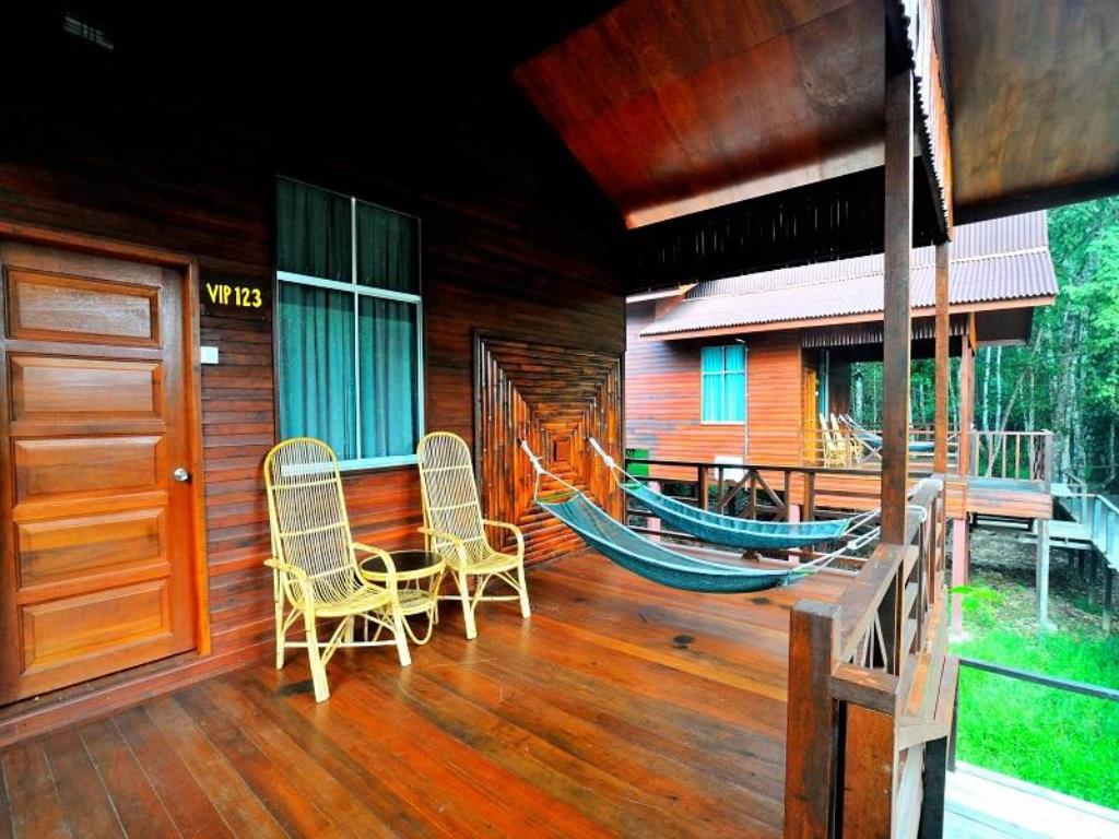 Wooden porch with chairs and hammock overlooking another cabin in a green setting.