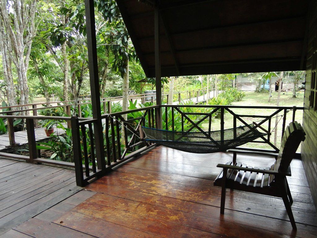 Wooden porch with a chair overlooking a lush green yard and trees.