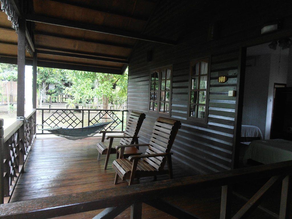 Wooden porch with two chairs, hammock, and building with windows overlooking a green landscape.