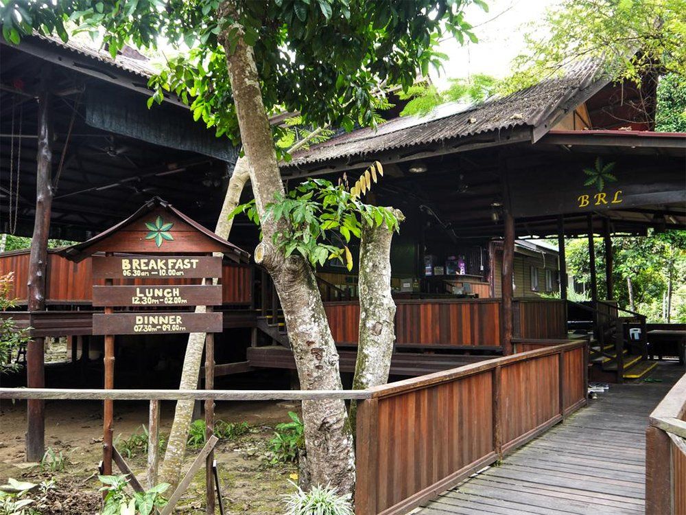 Wooden buildings with a walkway, surrounded by trees. Sign reads 