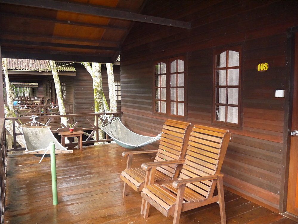 Wooden cabin porch with chairs, hammocks, and windows.