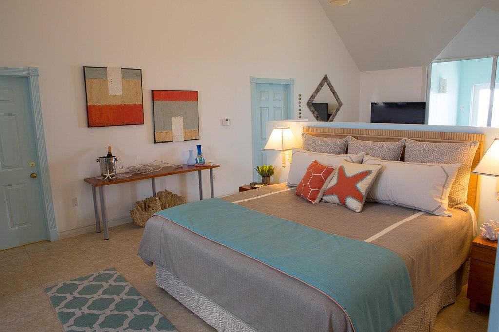 Bedroom with a bed, artwork, and a table. Coastal theme with blue, orange, and tan colors.