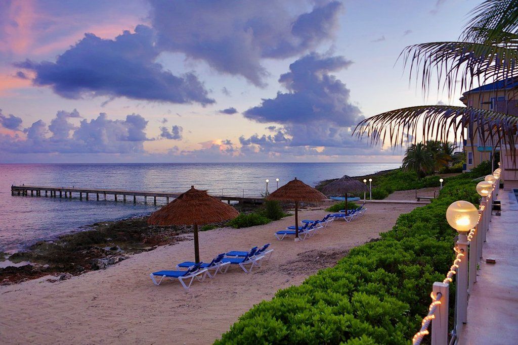 Beach at sunset with lounge chairs, thatched umbrellas, and pier.