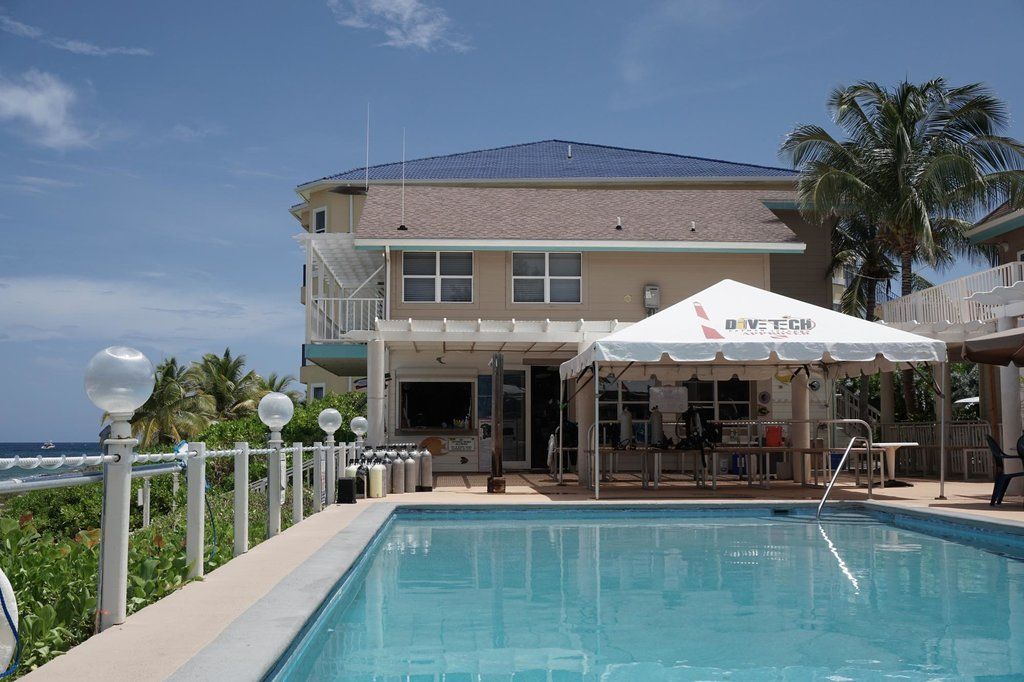 Two-story beige house with a pool, ocean view, and tent for shade under blue sky.