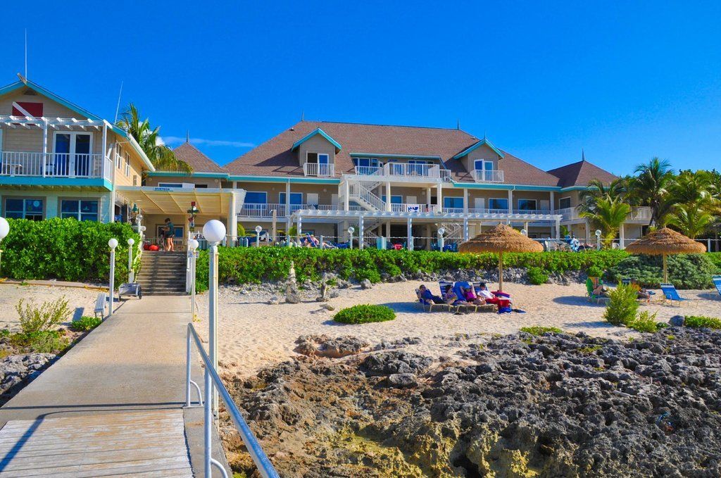 Beachfront resort with white balconies, wooden dock, turquoise water, and clear blue sky.