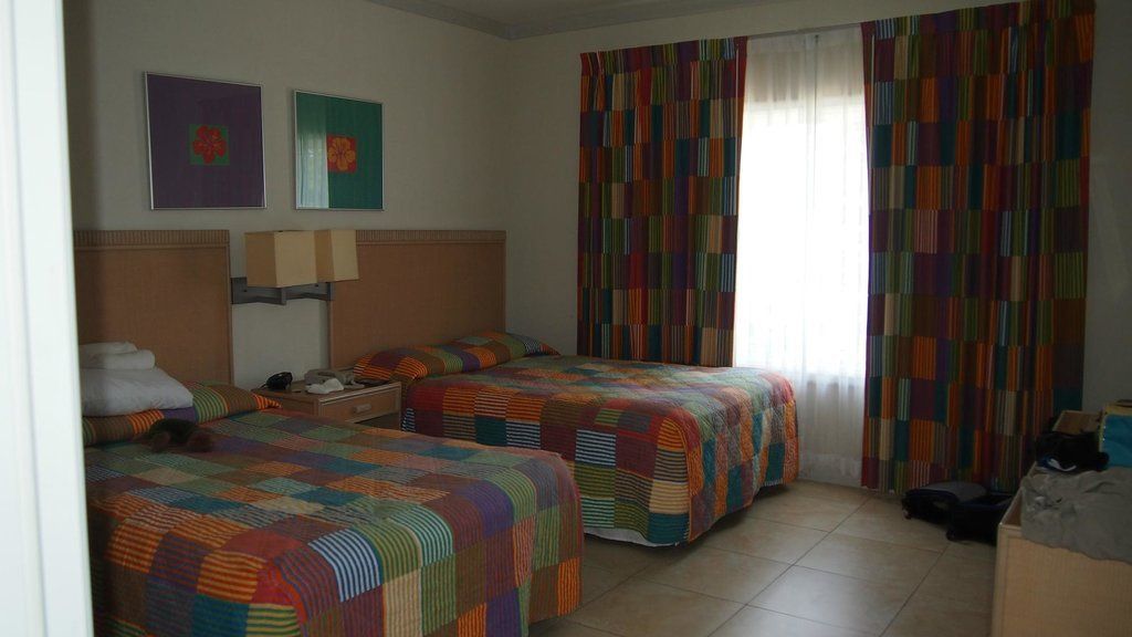 A hotel room with two twin beds, colorful patchwork bedspreads, curtains, and artwork on the wall.