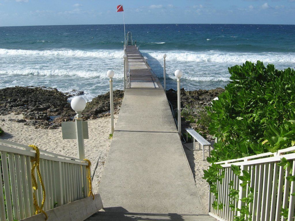 Concrete pier extends to ocean, flanked by white railings and small lights. Waves crash on shore.