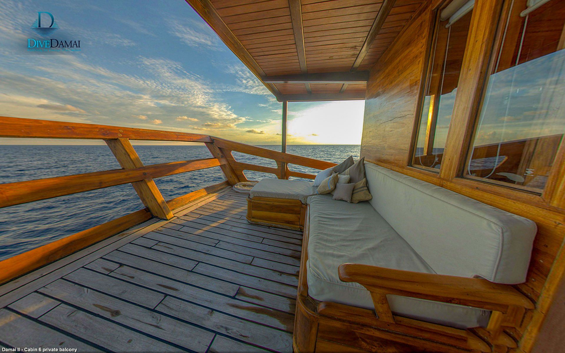Wooden boat deck with seating, ocean view at sunset.