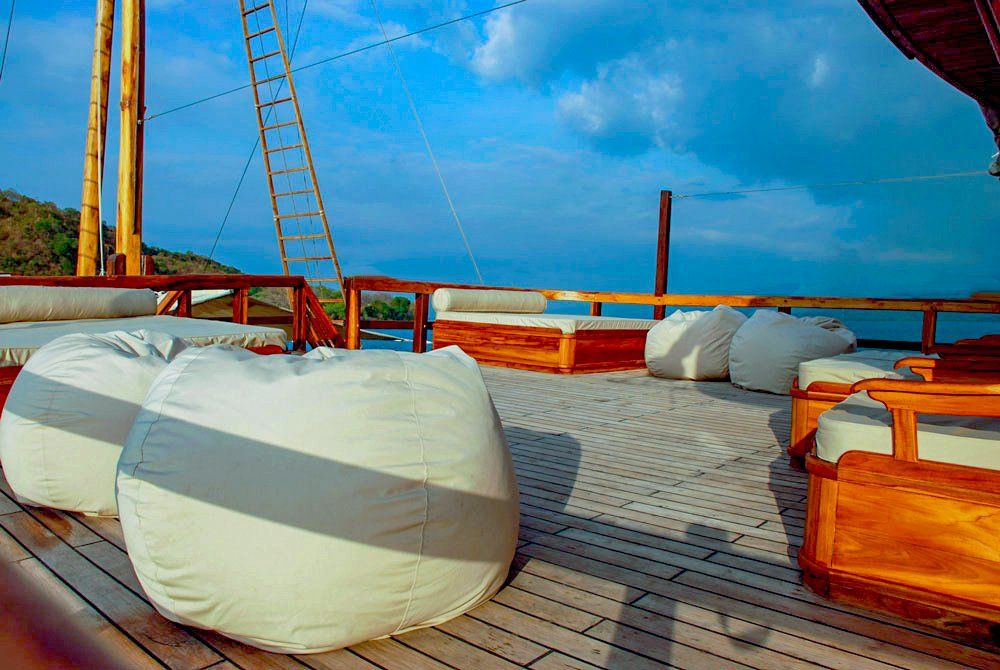 Wooden sailboat deck with beanbag chairs and cushions overlooking a blue sea and sky.