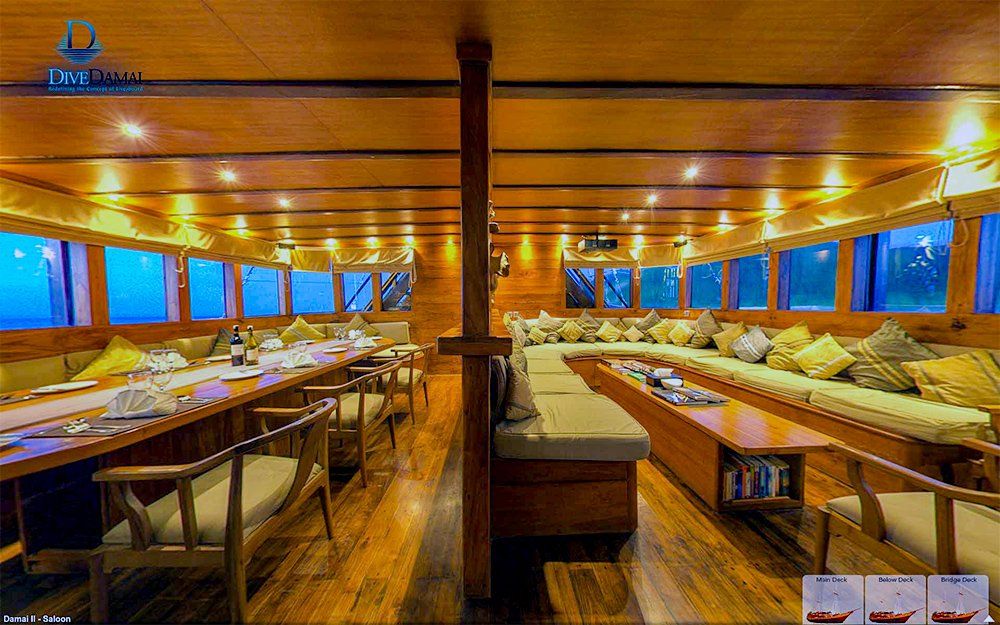 Interior of a wooden boat with dining tables and seating by windows. Warm lighting.