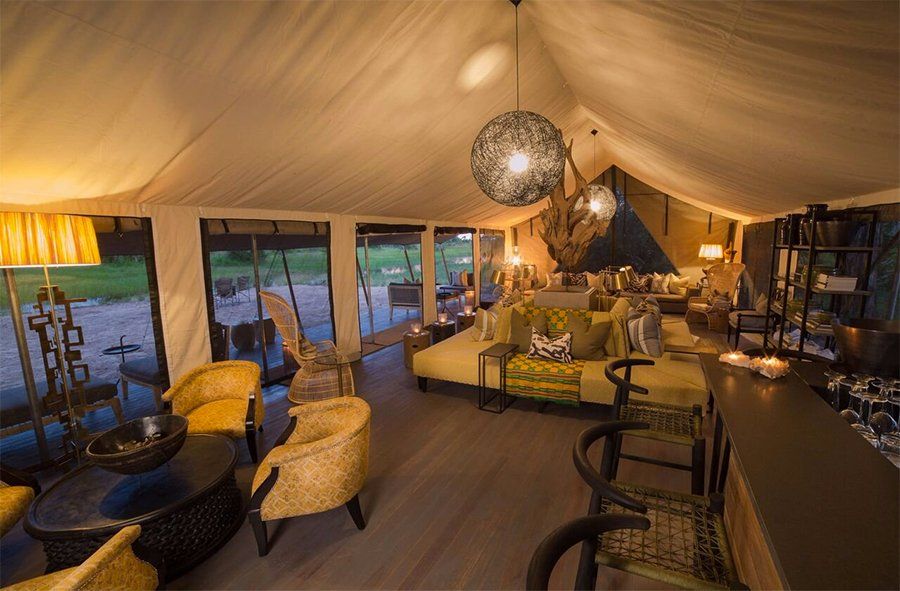 Interior of a safari tent lounge with seating, bar, and hanging lights.
