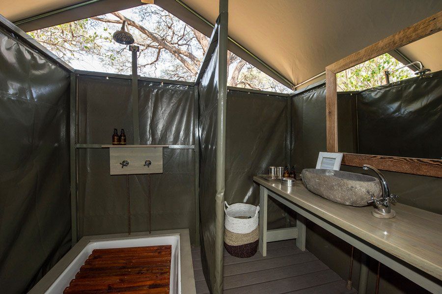 Outdoor shower and vanity in a tent, featuring a stone sink, wooden bathtub, and shower head.