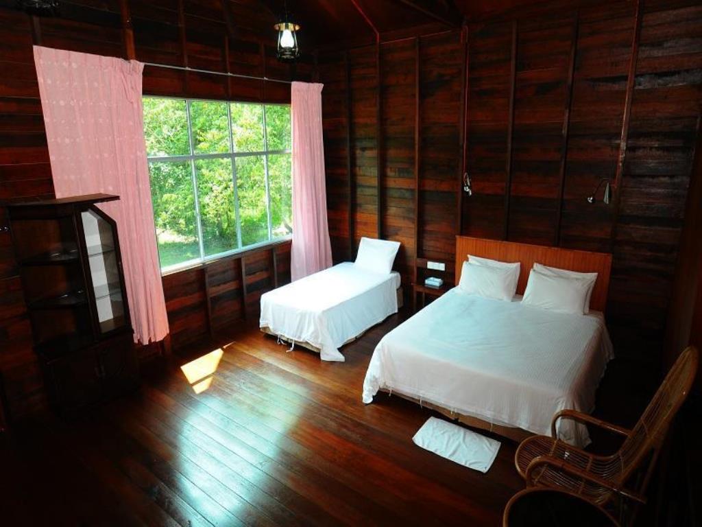 Wooden bedroom with two beds, a window with pink curtains, and a rattan chair.
