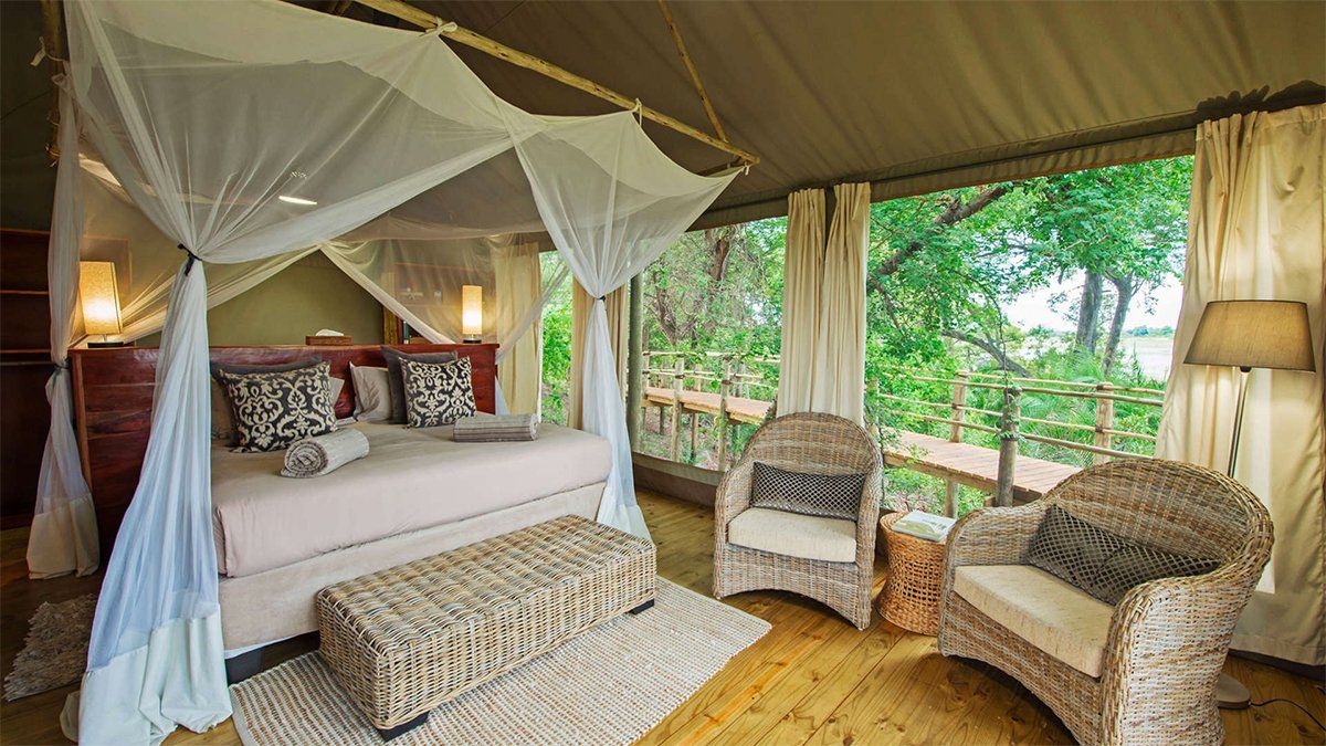 Safari tent interior with bed, seating area, and outdoor view.